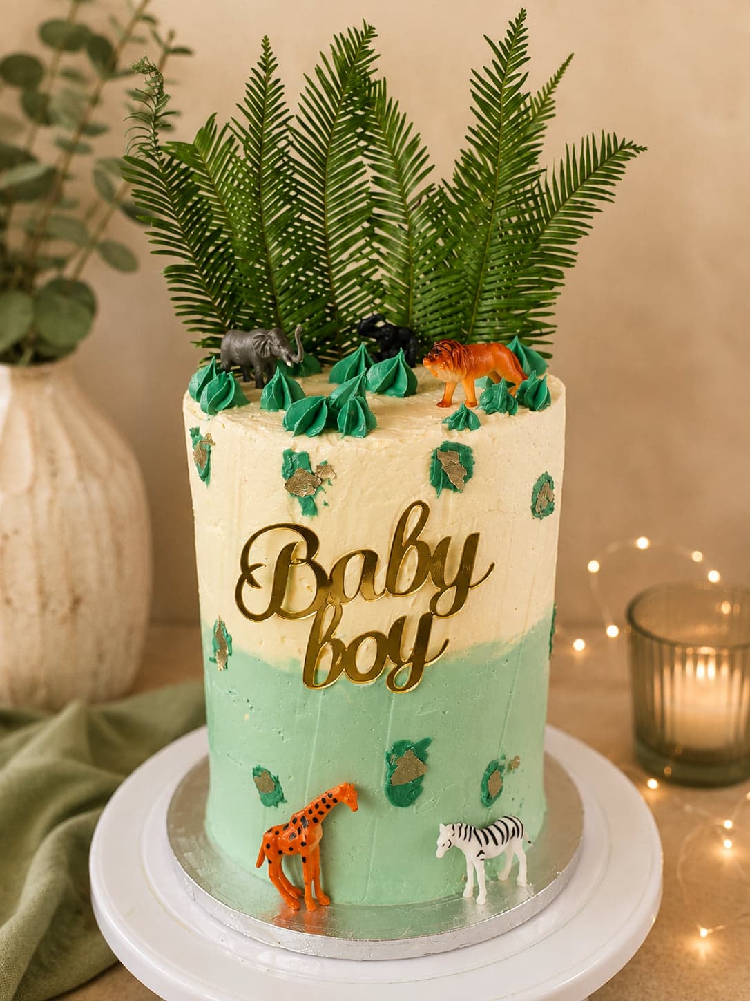 Babyshowertaart in crème en zachtgroen met varens, safaridiertjes en een gouden Baby boy-topper